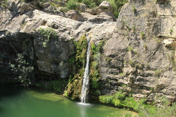 Waterfall flowing down rocky cliff into green pool, peaceful canyon nature scene
