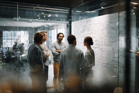 Diverse team brainstorming ideas on a glass whiteboard in a modern office