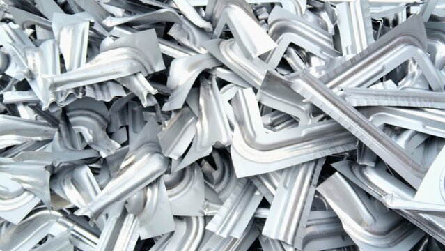 Pile of scrap metal pieces from industrial stamping process. Recyclable steel and aluminum waste in a factory environment.