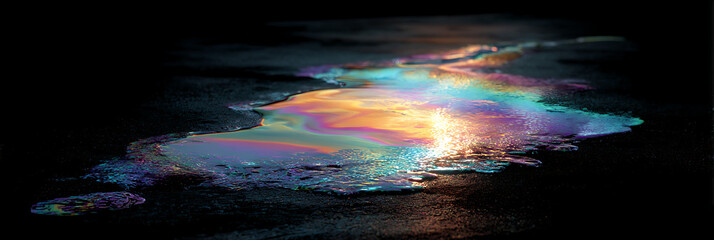 Fototapeta premium Iridescent oil slick shimmering on wet dark asphalt at night, reflecting vibrant rainbow colors under artificial city lights in a cinematic panoramic view.