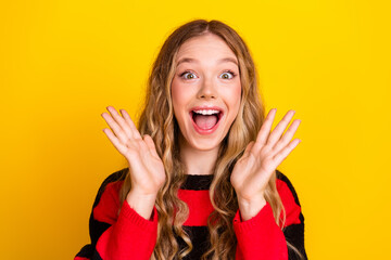 Cheerful young woman with joyful expression poses against yellow background in striped sweater...