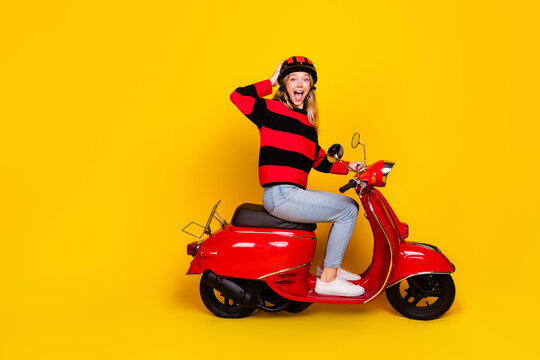 Charming Young Woman Posing on a Red Scooter with Cheerful Expression Against Vibrant Yellow Background