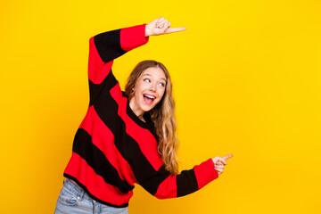 Cheerful young woman pointing up and away with happy excitement, wearing a stylish striped sweater...