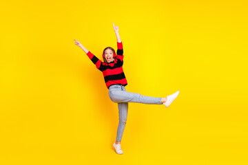 Cheerful young woman in casual striped sweater posing happily on a vibrant yellow background...