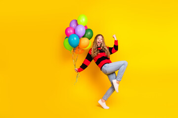 Cheerful girl holding colorful balloons while posing joyfully on a bright yellow background in...