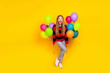 Lovely young girl holding colorful balloons on a cheerful yellow background, dressed in a stylish...