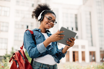 E-Learning. Happy Black Female Student Using Tablet Computer Wearing Headphones Standing Near...