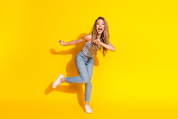 Excited young woman in trendy casual outfit leaping and smiling against vibrant yellow background