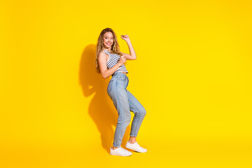 Smiling young girl poses joyfully against a vibrant yellow background in casual and stylish attire, representing happiness