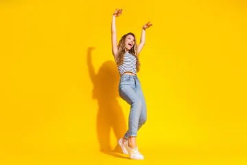 Fotobehang Onderzeeër Cheerful young woman in casual outfit leaping joyfully on a vibrant yellow background representing happiness, energy, and youthfulness.  © deagreez