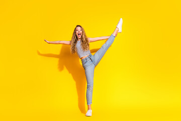 Young joyful woman in casual attire stretching energetically against a vibrant yellow background,...