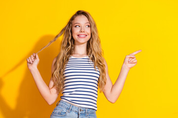 Charming young woman with long blonde hair smiling and making gestures against a vibrant yellow...