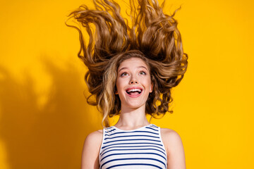 Excited blonde woman with wavy hair joyfully flipping her head on vibrant yellow background wearing...