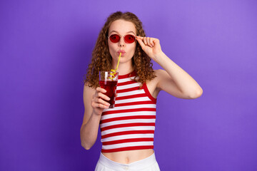 Young girl in red striped singlet sipping a drink with purple background wearing red sunglass for a...