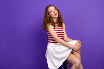 Obraz premium Young woman sits smiling in a red striped top and white skirt against a purple background casual fashion portrait