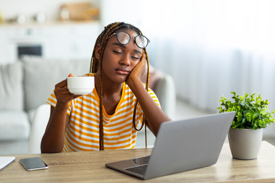 Exhausted millennial black woman freelancer sitting in front of laptop with cup of coffee, feeling sleepy and tired or hangover, suffering from burnout, working from home, copy space