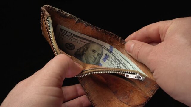 Hands opening a leather wallet to reveal cash inside, showcasing the zipper and interior details in a close-up shot