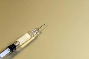 Glass syringe filled with transparent liquid lying horizontally on a soft yellow background, minimal medical still life symbolizing vaccination, cosmetic filler, insulin injection and healthcare. © Pat dream