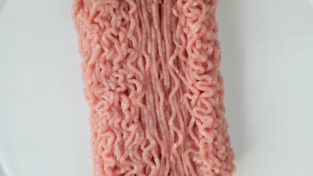 Fresh raw minced turkey meat rotating on a turntable isolated on a white background.