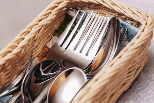 Cutlery set in wicker basket. Forks and spoons neatly stored together. Tableware organization detail. Clean metal utensils for dining and kitchen use. Closeup of everyday household items.
