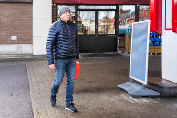 Errand autonomy older man walking with fuel container at gas station forecourt, winter jacket and knit hat, everyday refueling context for independent daily mobility routines. © Nimbus Works