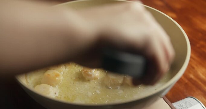 Woman cooking scallops at home in her kitchen, frying sea scallops in a pan on a portable gas stove. Close-up of scallops being turned to achieve an even golden sear, homemade seafood cooking process