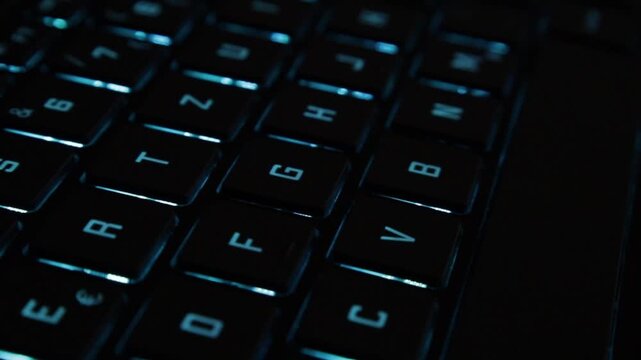 slide view over blue glowing notebook computer keyboard technology in darkness