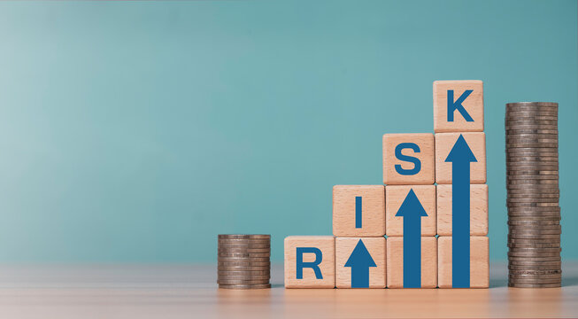 Investment risk and financial concept with wooden blocks forming rising arrows and word risk, next to stacked coins for related of business risk and profit return concept.