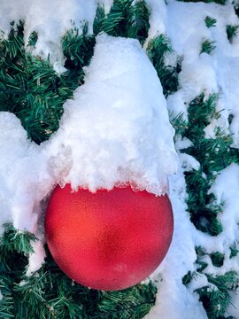 Close-up of festive red Christmas bauble hanging on a fir tree covered with snow