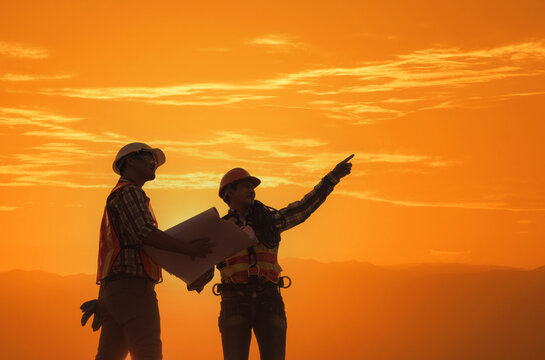 Silhouette of Two construction workers looking at plans on a construction site at sunset, Thailand