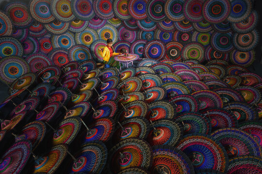 Young Burmese woman sitting on a stool in a workshop making traditional colourful Pathein Umbrellas (Pathein hti), Myanmar