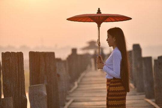 Side view of a young Woman carrying a traditional parasol standing on U Bein Bridge, Amarapura near Mandalay, Myanmar