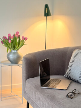 Close-up of an open laptop computer with a blank screen and pair of glasses on a sofa with cushions in a living room