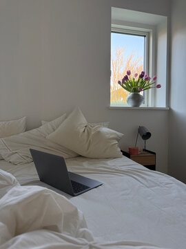 Open laptop computer on an unmade messy bed in a bedroom