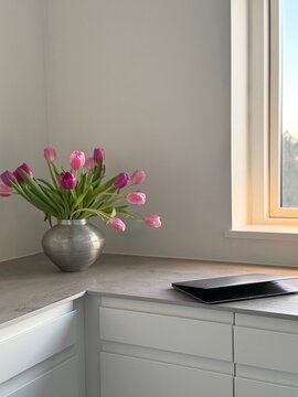 Close-up of a laptop computer on a kitchen worktop next to a vase with pink tulips
