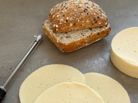 Close-up of a fresh bread roll with butter, sliced cheese and a cheese slicer  on a kitchen worktop