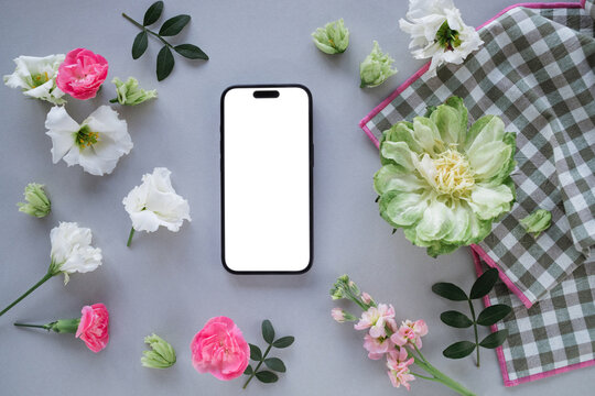 Close-up of a mobile phone with a blank screen on a table with assorted flowers and a napkin