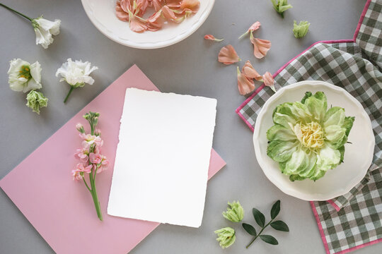Close-up overhead view of a blank deckle edge card and notebook on a table with assorted flowers and a napkin