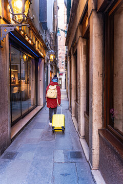 Rear view of a Teenage boy walking through the streets pulling a carry on suitcase in winter, Venice, Veneto, Italy