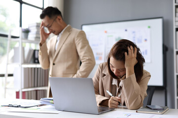 Obraz premium Young stressed businesswoman with listening to her angry manager complaining about work while sitting at office desk in front of laptop.