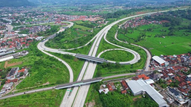 Aerial drone footage of a new big motorway interchange, on the side of Sumedang city, in Java island, Indonesia, inside it's valley of mountains, in a cloudy atmosphere, with villages around