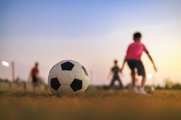 Obraz premium Soccer ball on green grass field with blurred silhouette of children playing football. Kids sport training concept.