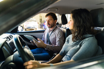 Young woman taking her driving exam and learning to drive vehicle assisted by her teacher, sitting inside modern car