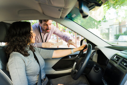 Male driving instructor explaining road safety to adult student learning to maneuver car during lesson