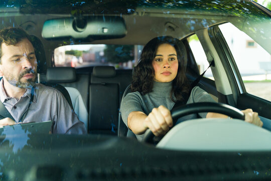 Nervous woman learning driving skills with male instructor assessing her progress on the road during a car lesson