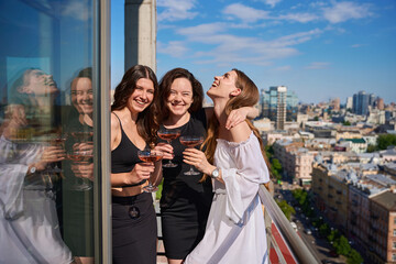 Naklejka premium Happy young women with glasses of champagne having party on terrace outdoors
