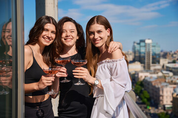 Naklejka premium Smiling young women posing with glasses of champagne on terrace outdoors