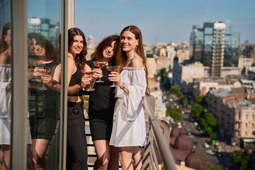 Naklejka premium Happy women standing on a rooftop holding glasses with champagne