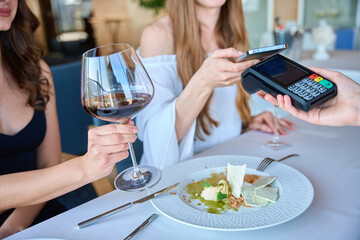 Young woman paying with smartphone to waiter in restaurant