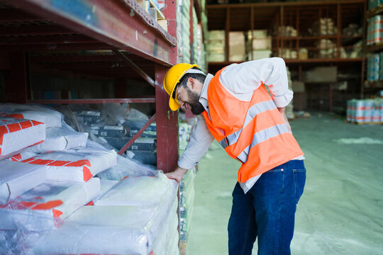 Industrial worker experiencing back pain while lifting heavy bags in a warehouse, suffering work-related injury